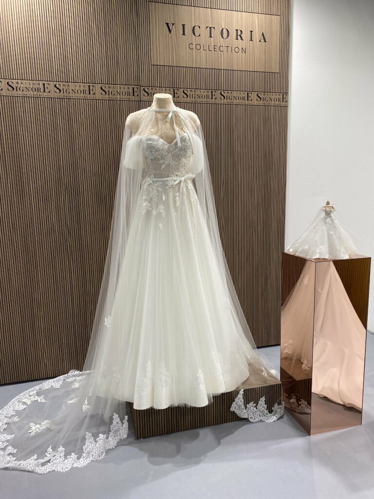 Foto de un vestido de novia blanco con velo de encaje tipo capa y un lazo en la cintura de Maison Signore y una miniatura del vestido