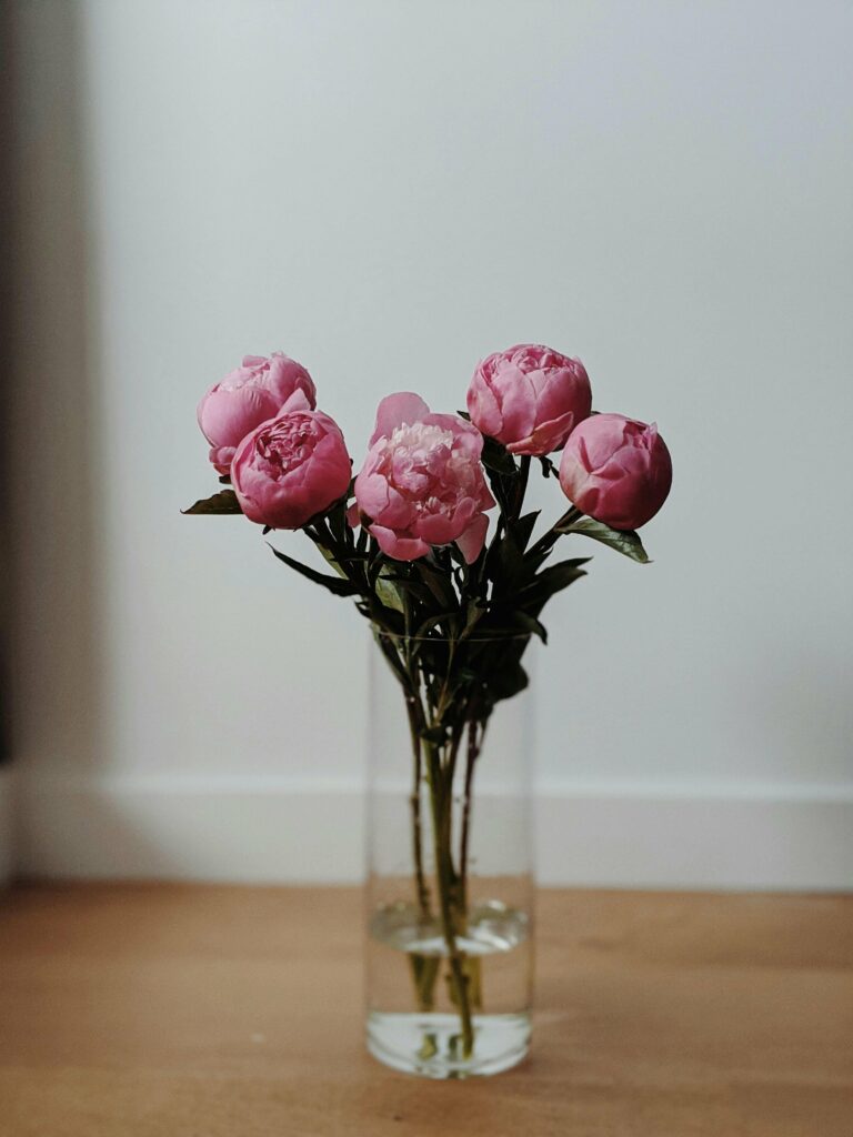 Foto de jarrón con peonias de color rosa sobre un suelo de madera