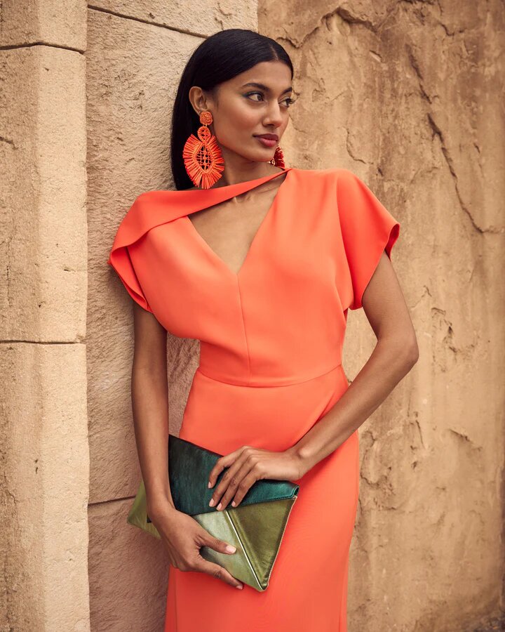 Foto de modelo con vestido den color naranja claro y colso pochette en color verde y oro en las manos